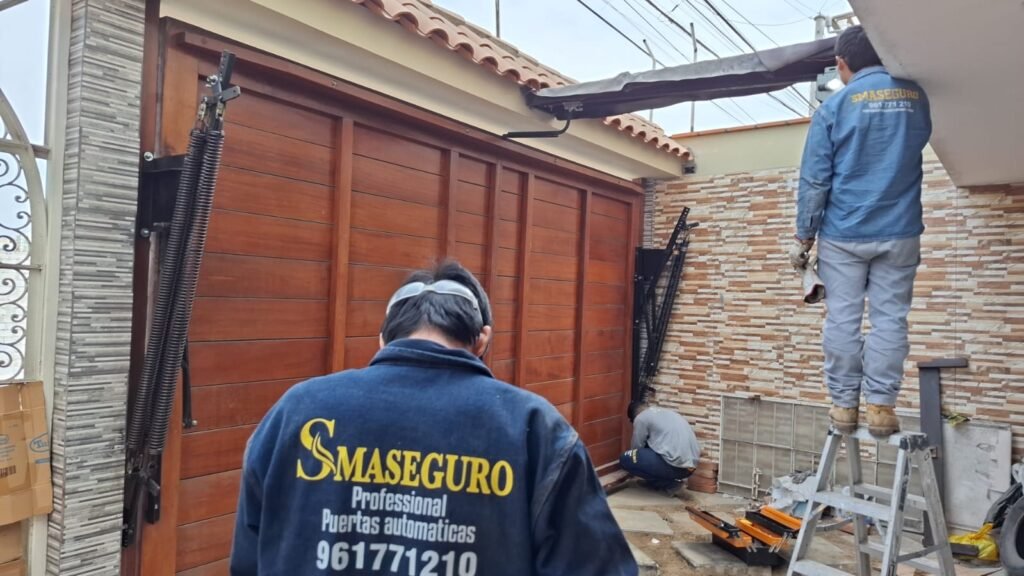 Técnico de Smaseguro instalando puerta levadiza de madera automatizada en cochera residencial.