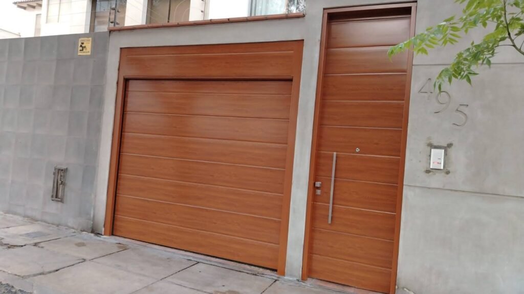 Puerta seccional color madera con puerta peatonal independiente instalada en fachada moderna en Lima.